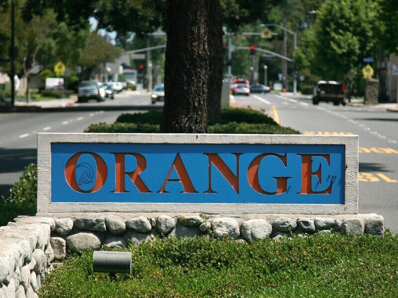 Welcome sign for the City of Orange, California, along a tree-lined street.