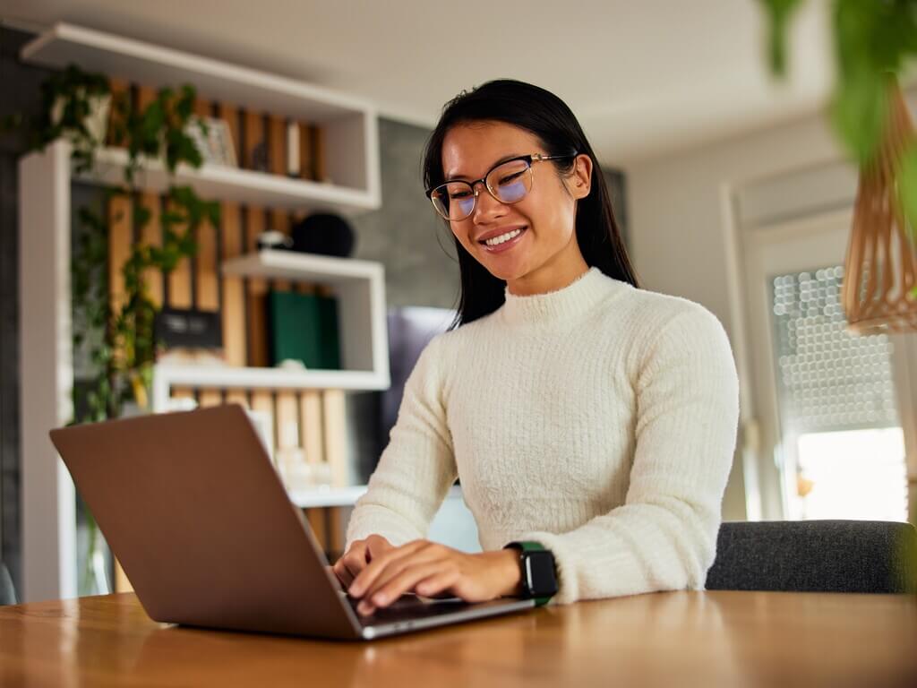 Smiling educator or nonprofit staff member working on laptop in a bright home office setting.