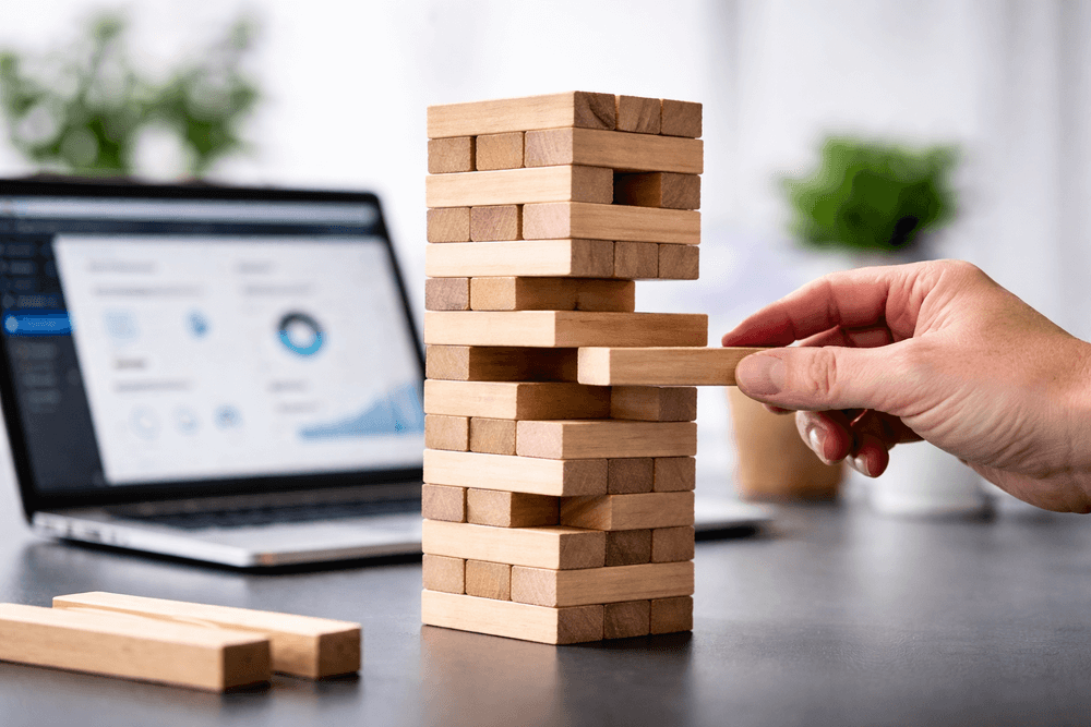 Hand pulling block from wooden tower on desk representing WordPress maintenance and plugin instability